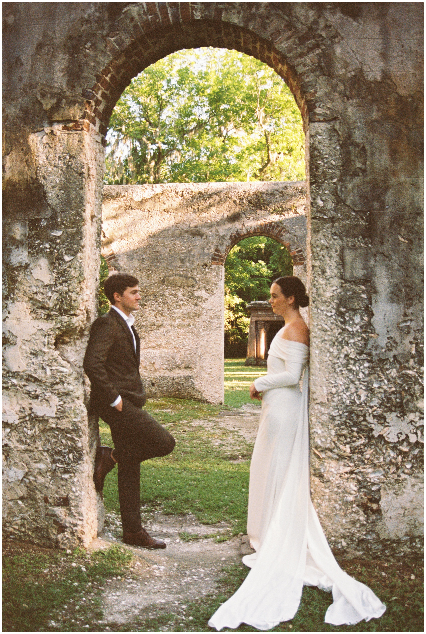 Newlyweds lean in a limestone arch in a park during their Charleston Elopement