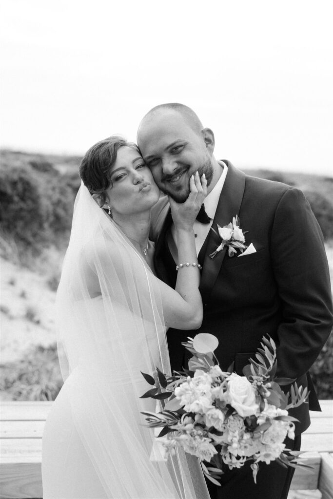 Happy newlyweds play and make silly faces on a beach boardwalk