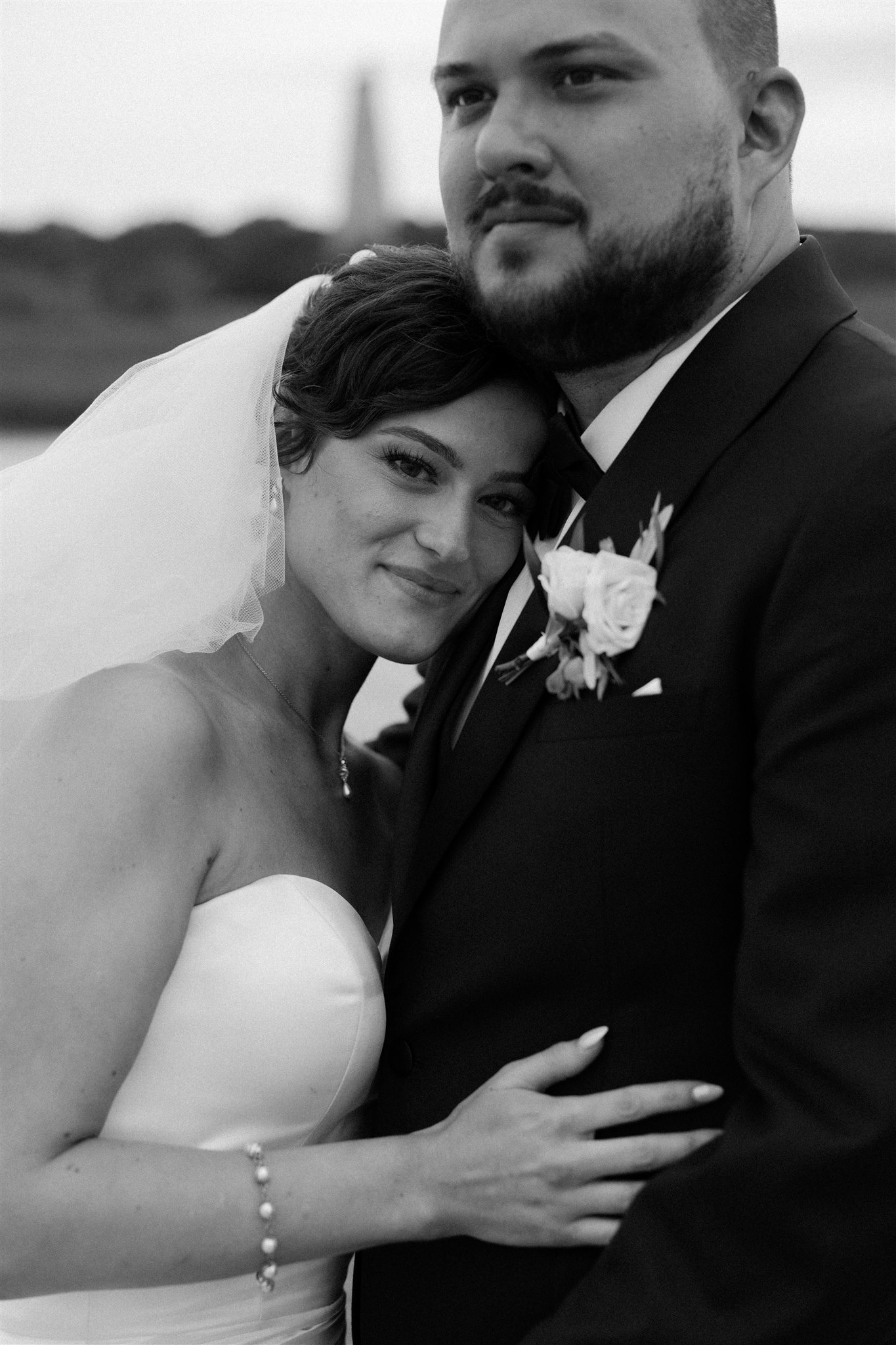 A bride smiles while leaning on the chest of her groom in balck and white at their choice of Charleston wedding venues