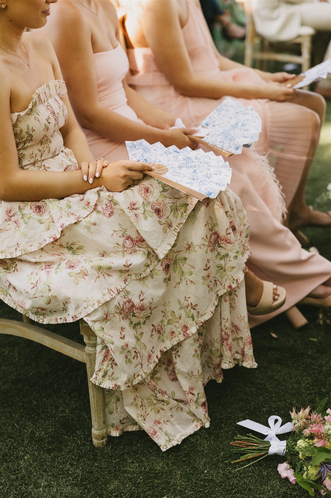 A group of women at a wedding ceremony in colorful dresses with floral print fans in their laps