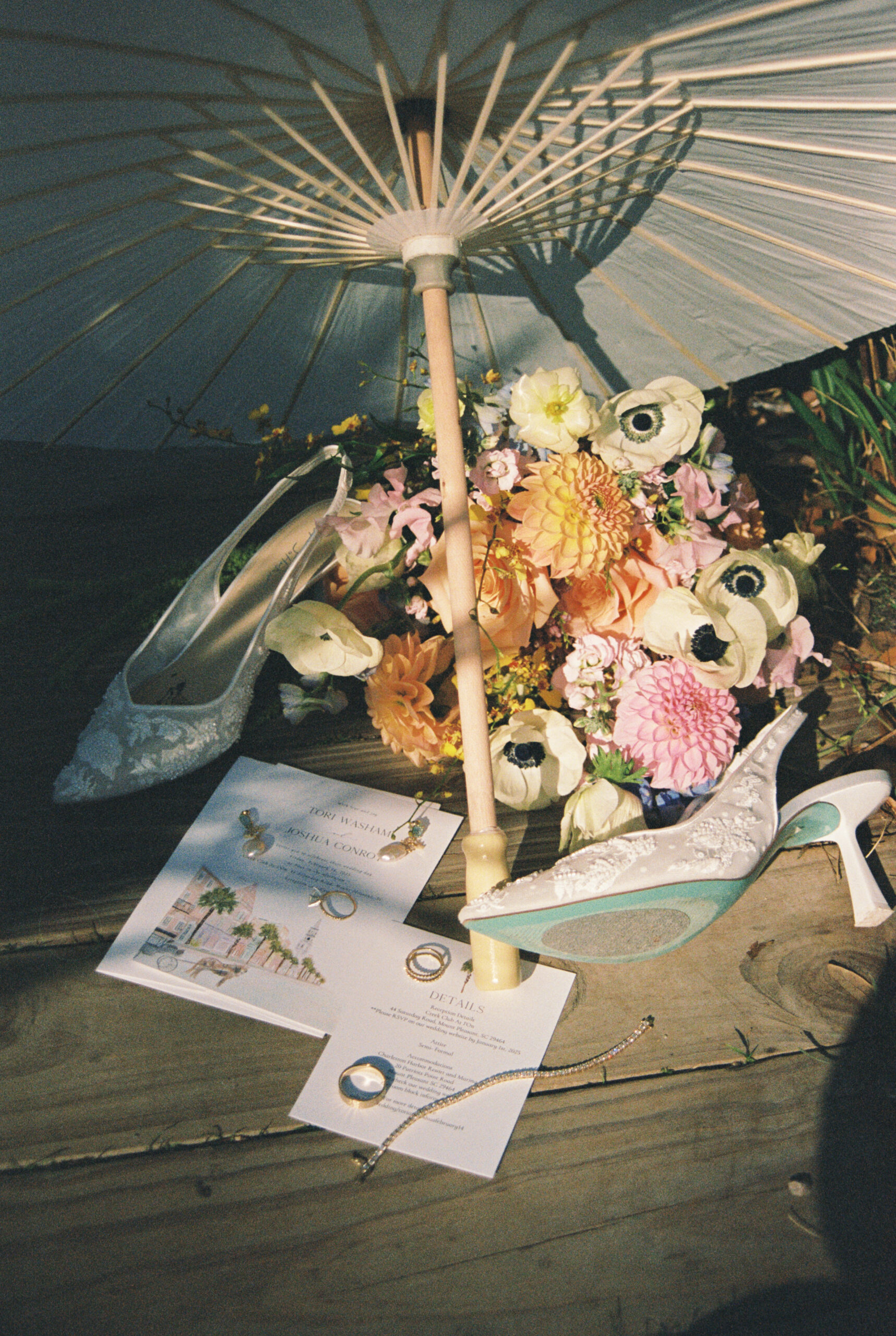 Bridal details with jewelry, shoes and bouquet sit under a parasol on a deck