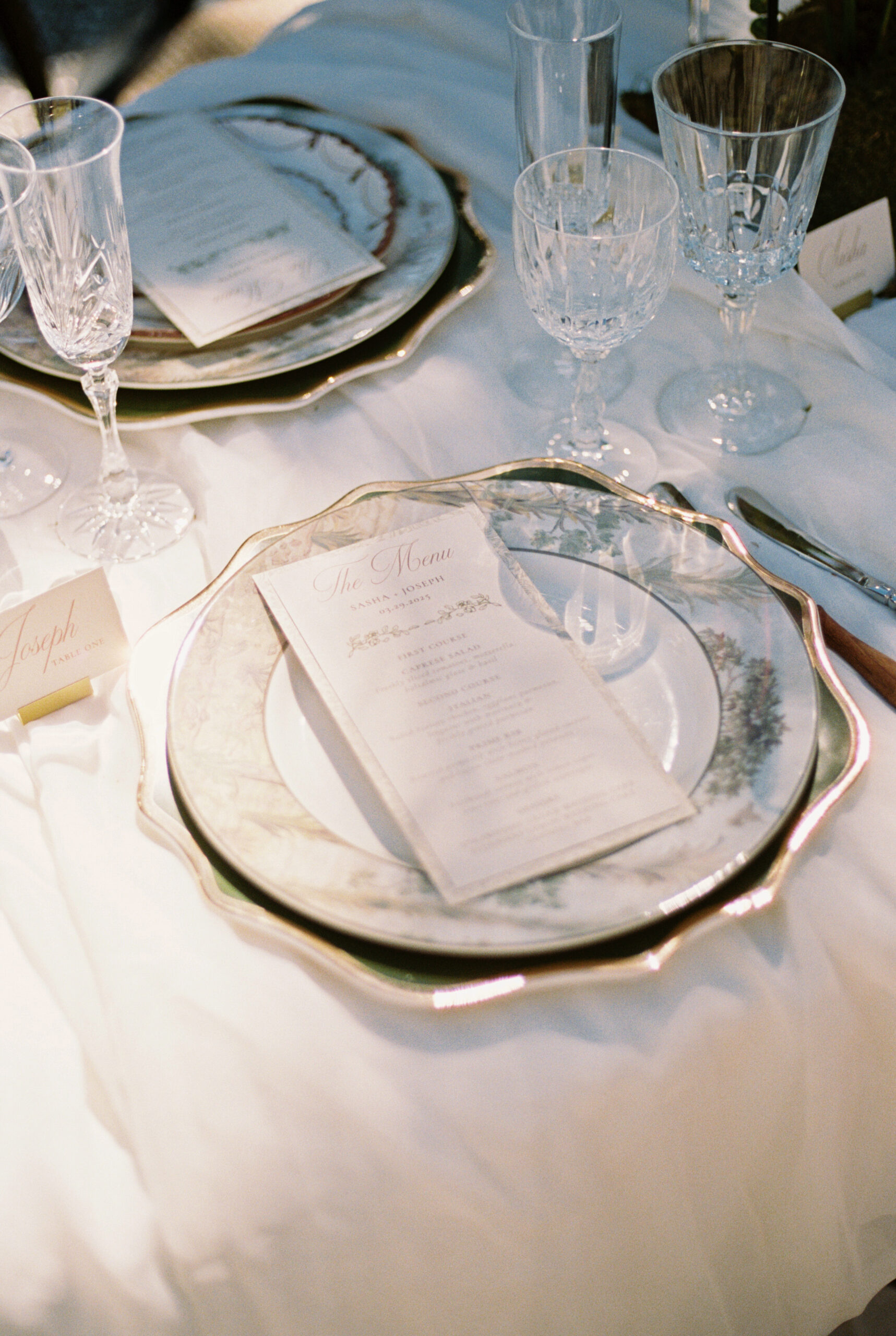 Details of a menu on a reception table setting with crystal glasses and ornate china plate