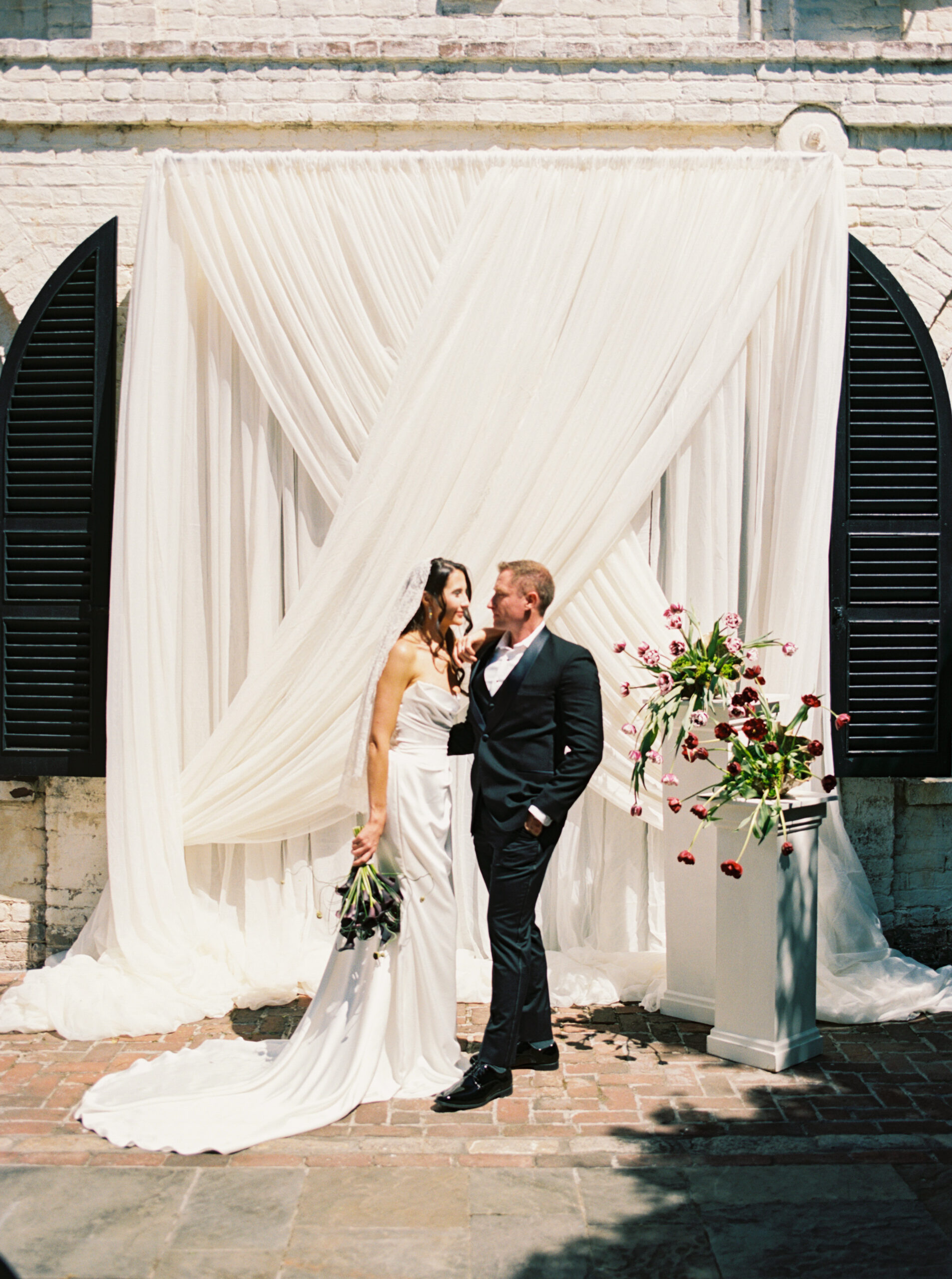 A bride and groom smile at each other while standing on a brick patio for their ceremony