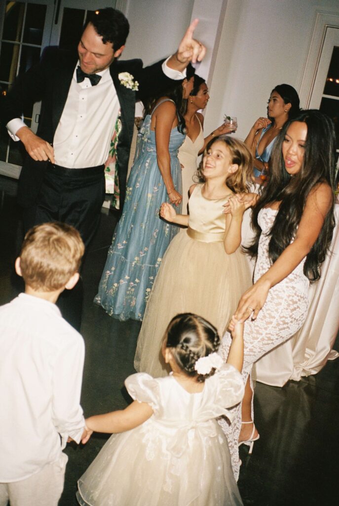 Newlyweds dance with three young children on the dance floor during their merrimon wynne house wedding reception