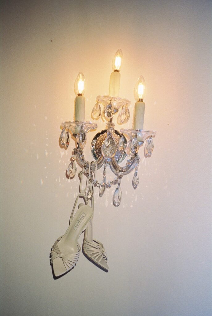 Details of a bride's shoes hanging from a crystal and candle sconce