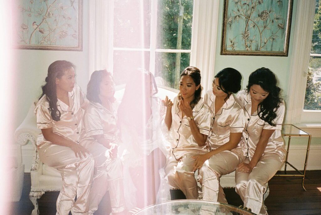 A bride sits with her bridesmaids on a couch in pink pajamas with a large sunflare
