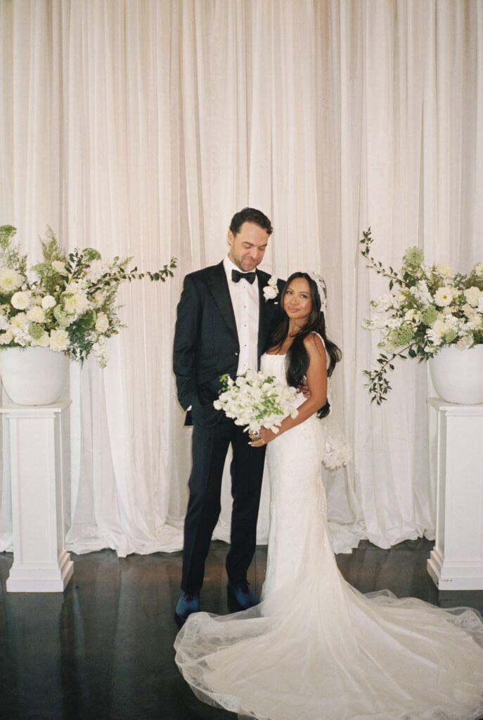 Newlyweds stand at their ceremony location smiling with white flowers
