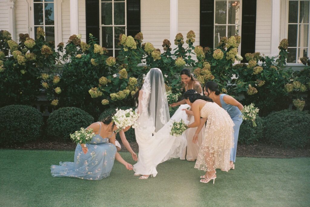 Bridesmaids help the bride adjust her train in the gardens