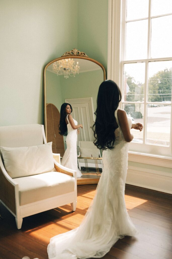 A bride admires her dress in an antique mirror while getting ready for her merrimon wynne house wedding