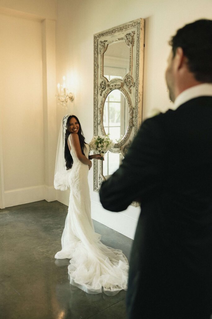 A happy bride turns to see her groom while standing in an ornate mirror at the merrimon wynne house wedding