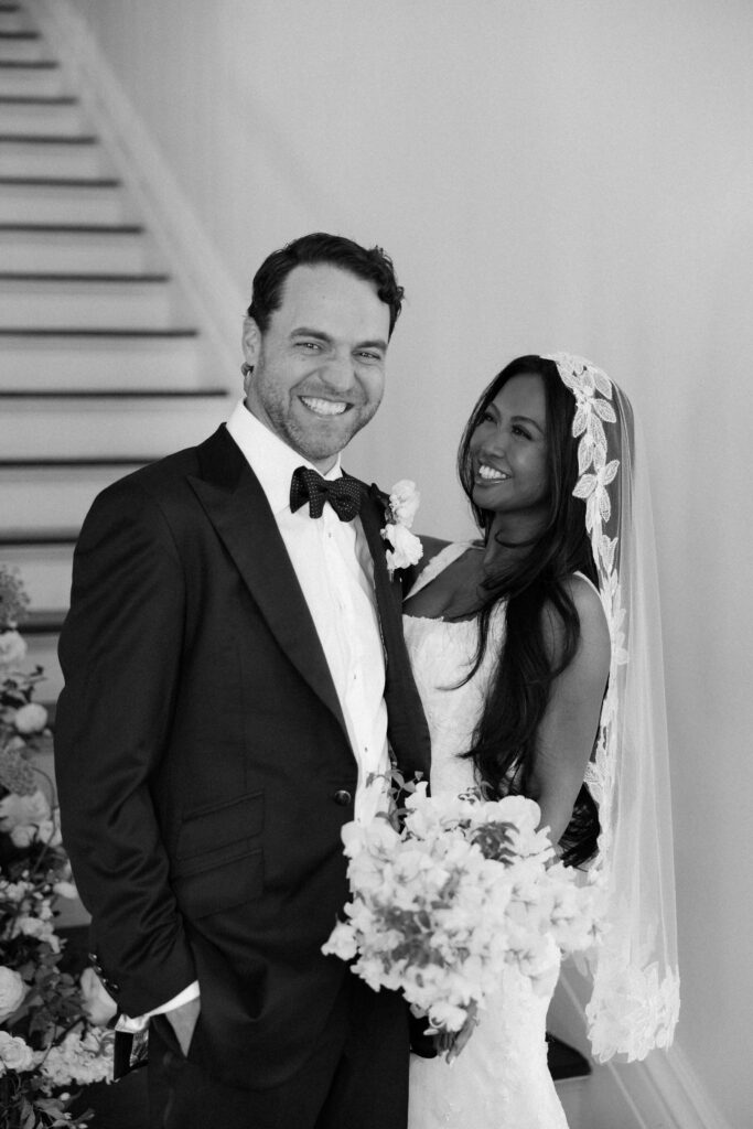Black and white image of newlyweds laughing on the grand staircase of the merrimon wynne house wedding venue