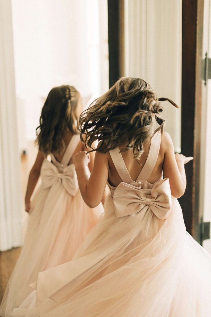 Two young girls in pink dresses run in a hallway