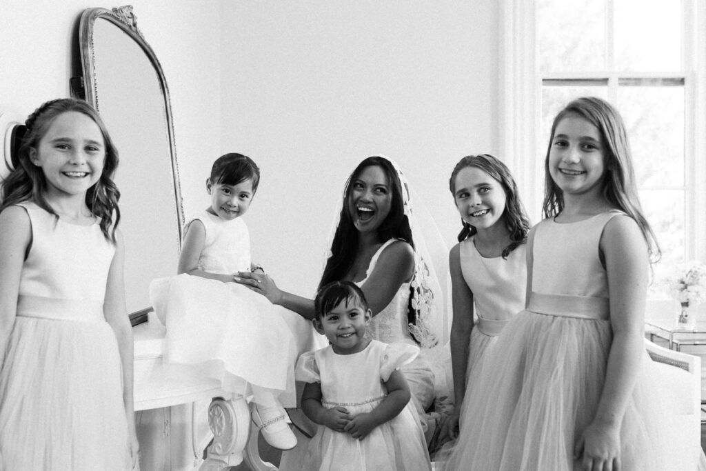 A bride laughs while playing with 5 young girls in her getting ready room