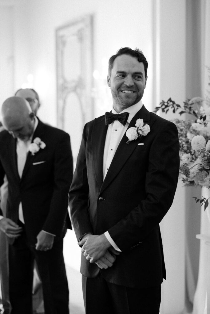 A happy groom awaits his bride at the altar in black and white