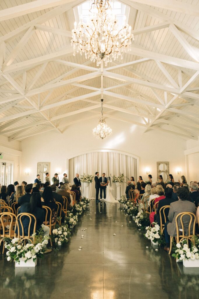 Newlyweds stand at the altar under chandeliers during their merrimon wynne house wedding ceremony