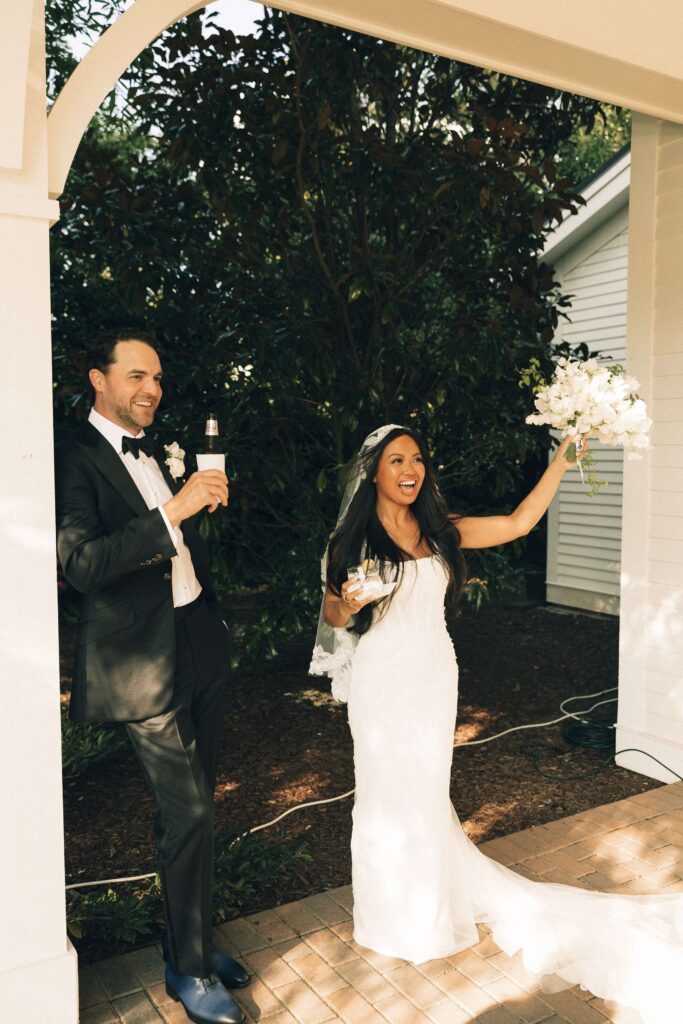 A bride and groom raise their drinks and bouquet on the patio