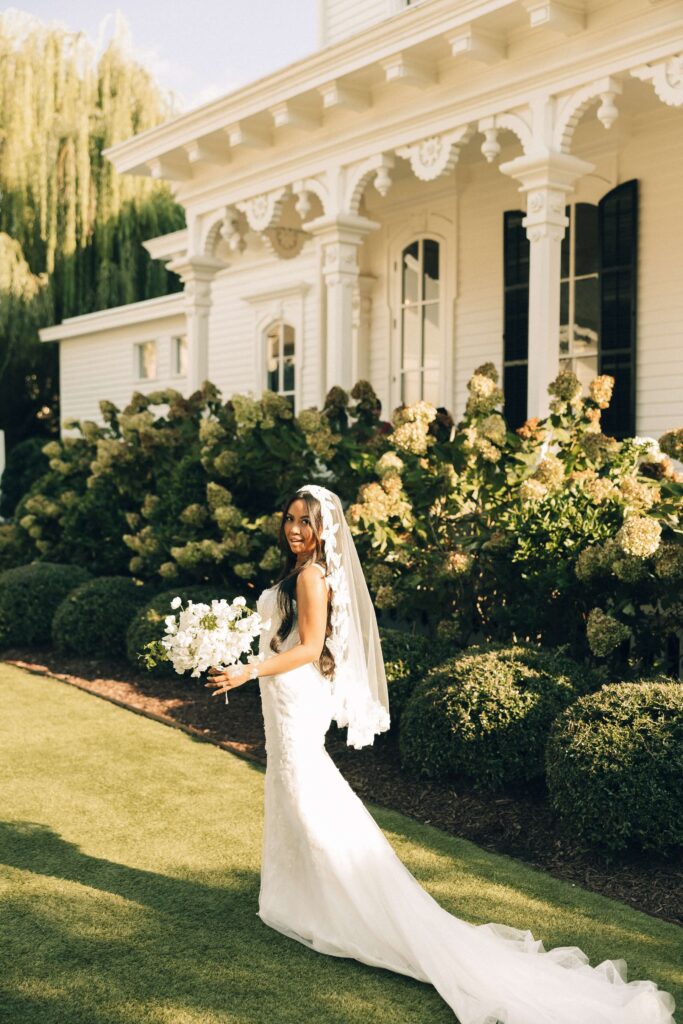 A smiling bride looks over her shoulder while walking the gardens of the merrimon wynne house wedding venue