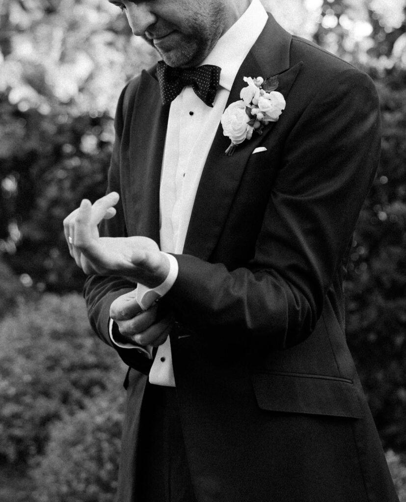 A groom buttons his cufflinks in the gardens while getting ready