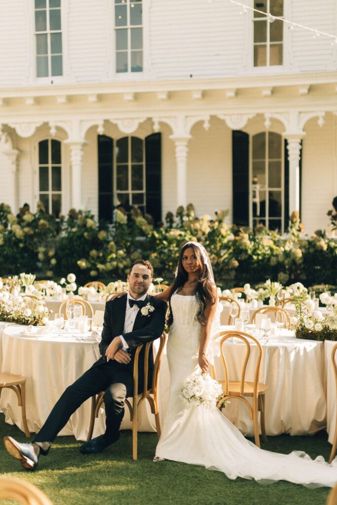 Newlyweds sit in the merrimon wynne house wedding venue lawn at their outdoor reception tables