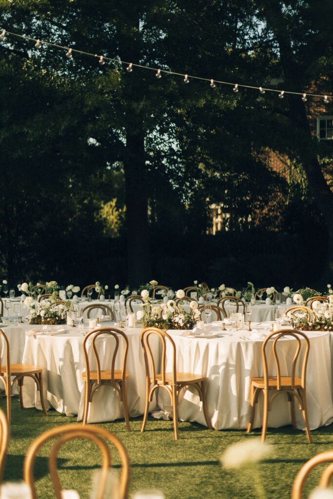 Details of an outdoor reception set up with white flowers and wooden chairs in the lawn of the merrimon wynne house wedding venue