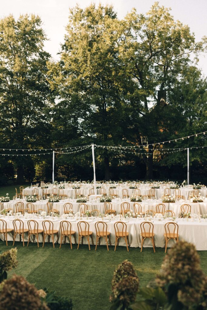 A set up merrimon wynne house wedding reception outdoor in the lawn with white linens and market lights