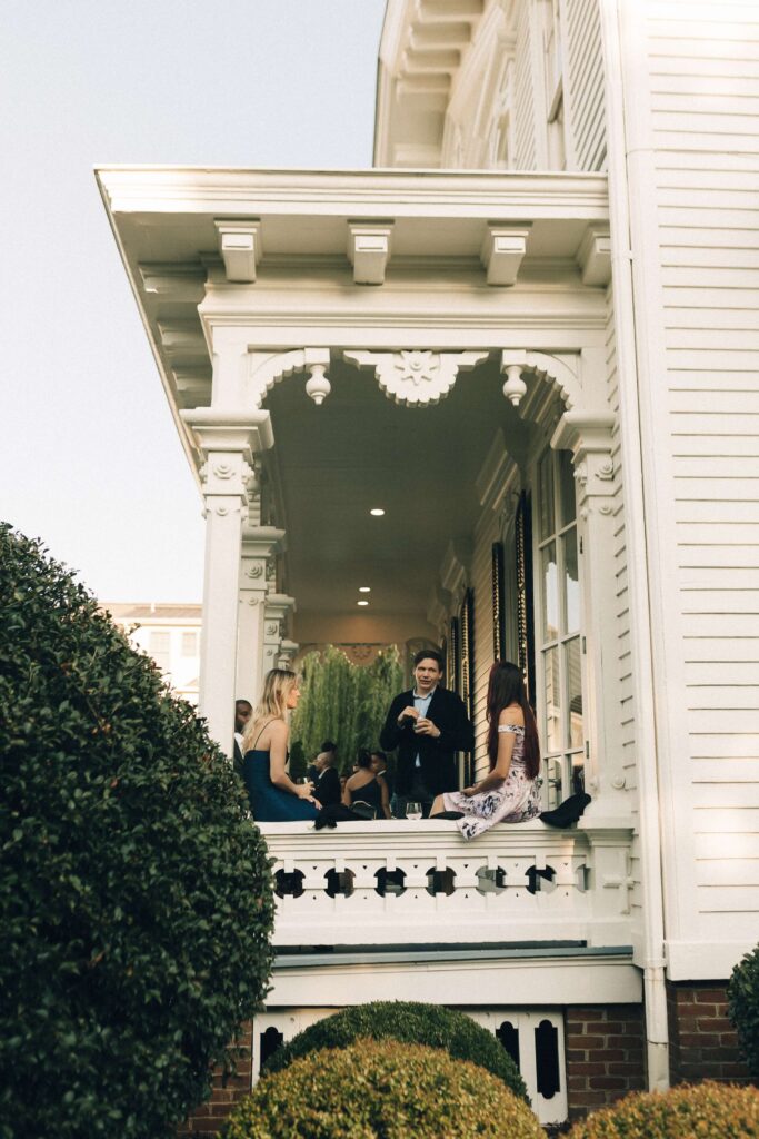 Wedding guests mingle on the front porch of the merrimon wynne house wedding venue during cocktail hour