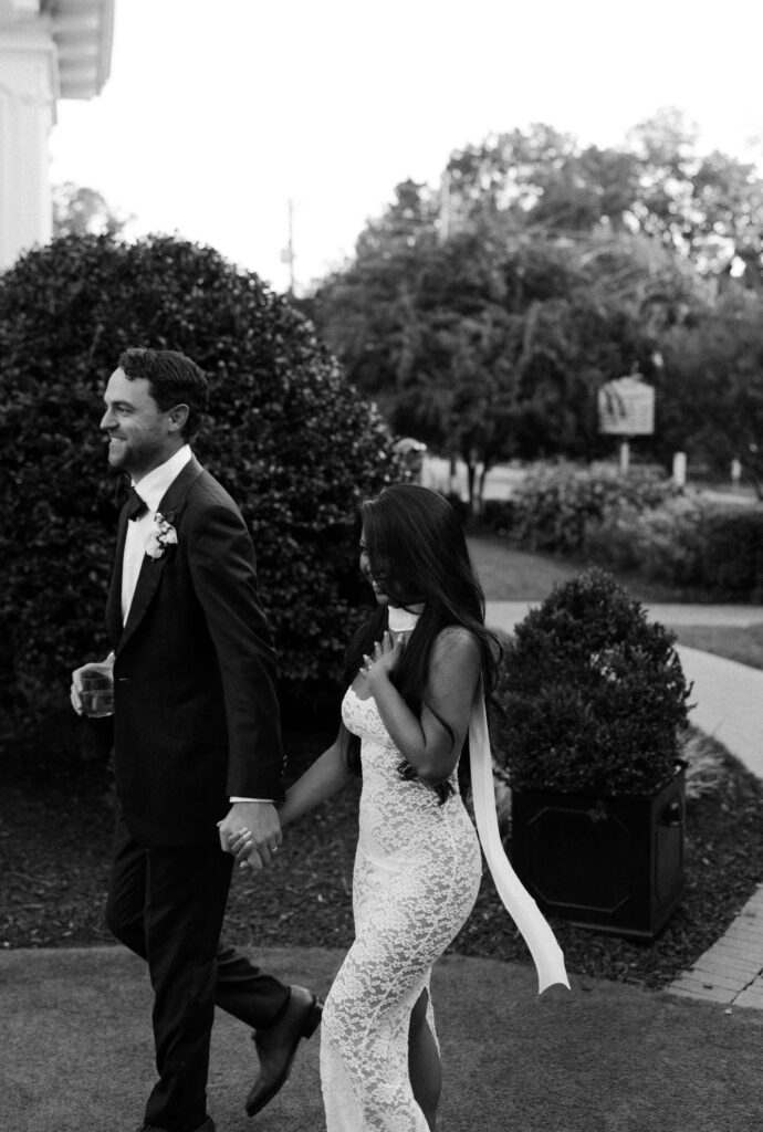 A bride and groom walk in the lawn holding hands and drinks at the merrimon wynne house wedding venue