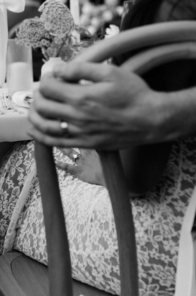 Details of a bride's ring hand on her lap while sitting in a wooden chair
