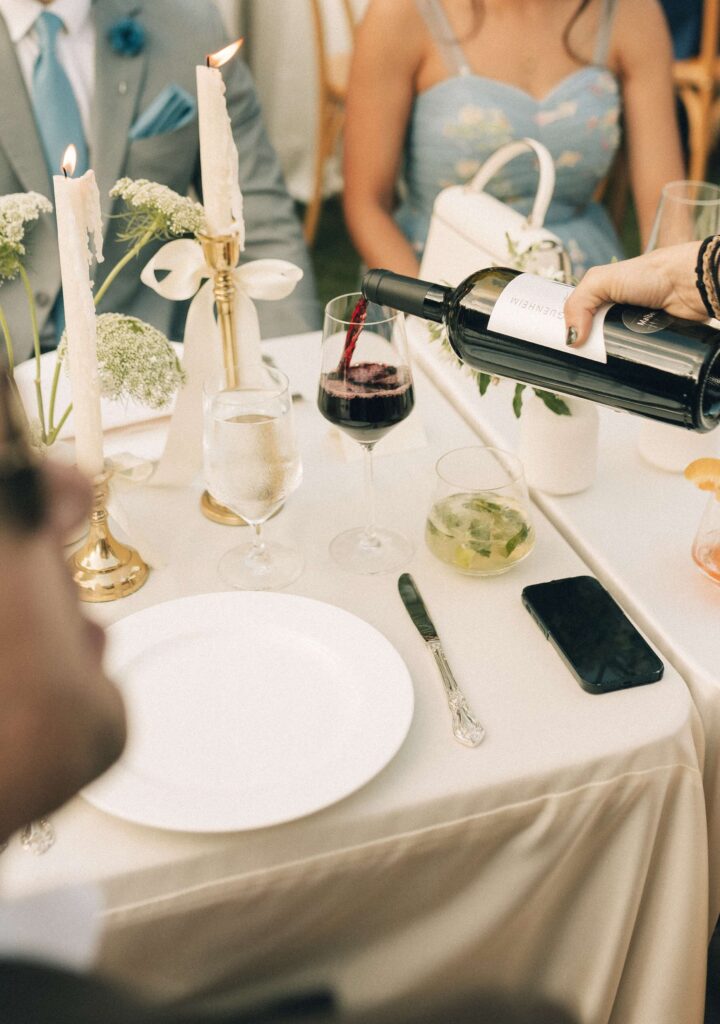 Details of someone pouring a glass of red wine at a reception table