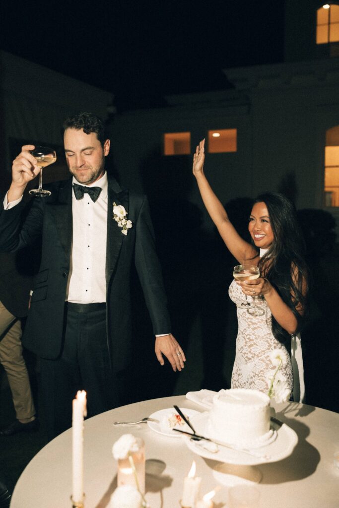 Newlyweds celebrate cutting their cake with drinks outdoors