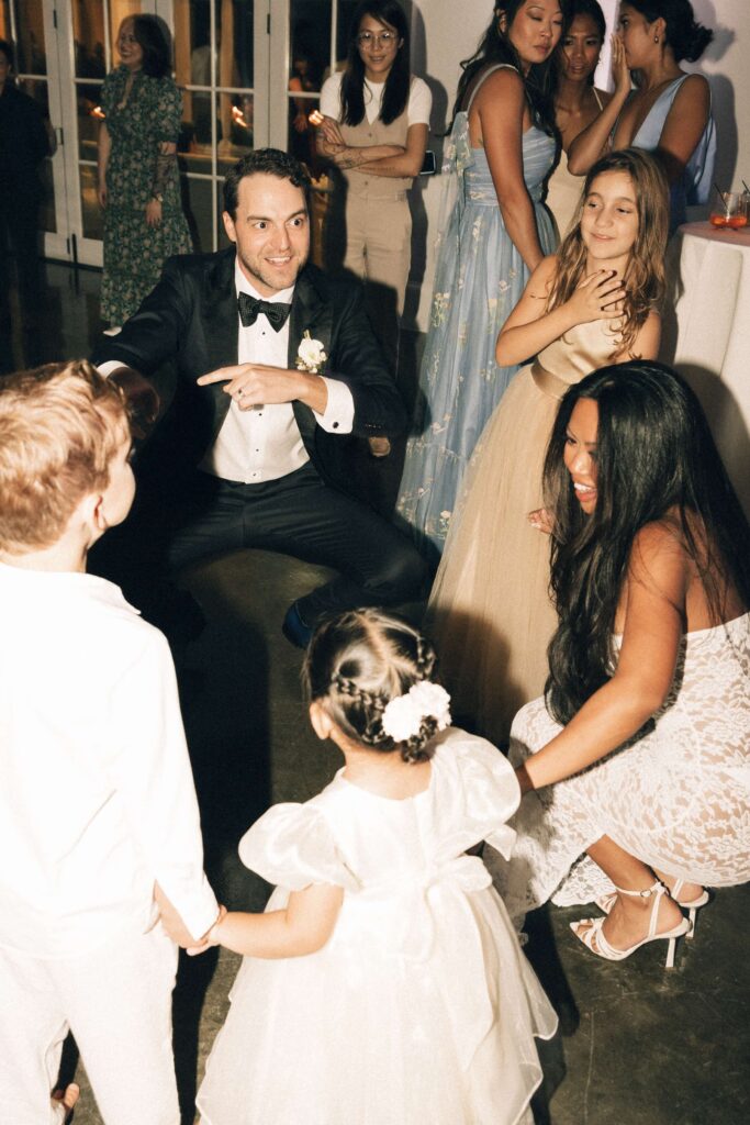 A bride and groom dance with some children on the dance floor