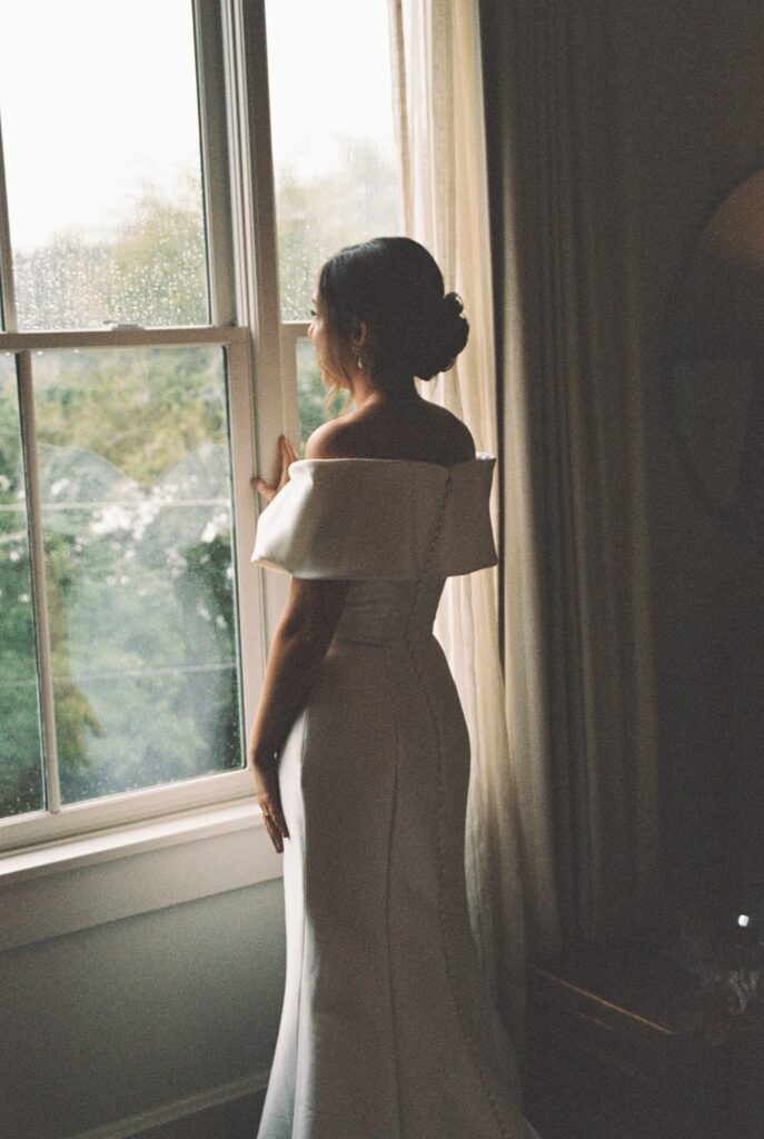 A bride peers out a window in her gown at the Post House Inn wedding venue