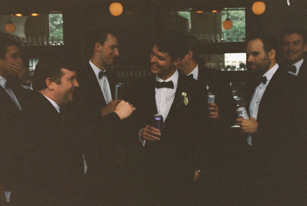 A laughing groom with his groomsmen in all matching black tuxedos at the Post House Inn wedding venue bar