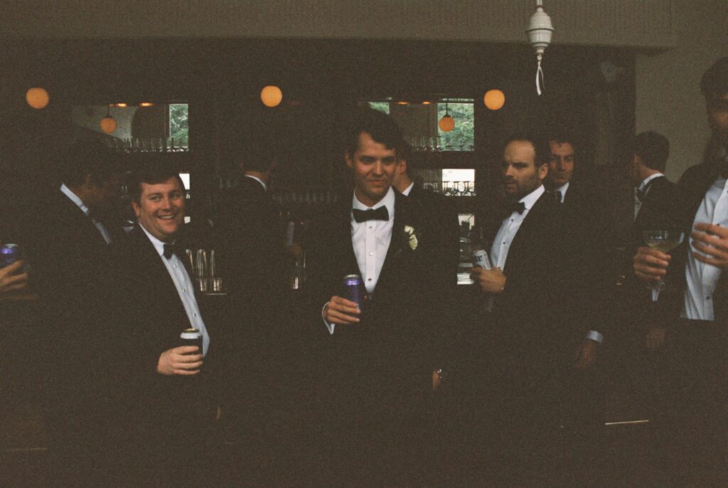 A groom laughs with groomsmen in black tuxedos at the bar