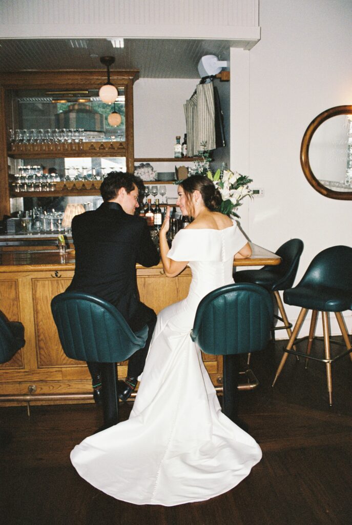 A bride shows off her ring to her groom as they sit at the bar