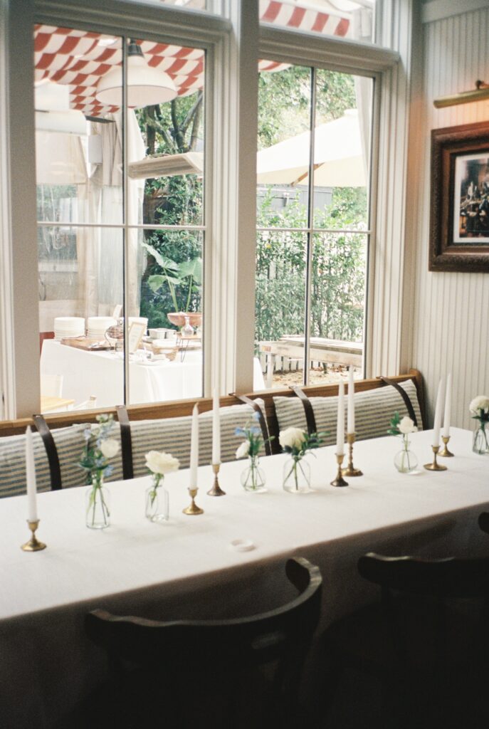 Details of a long reception table set up with candles and white florals under a window