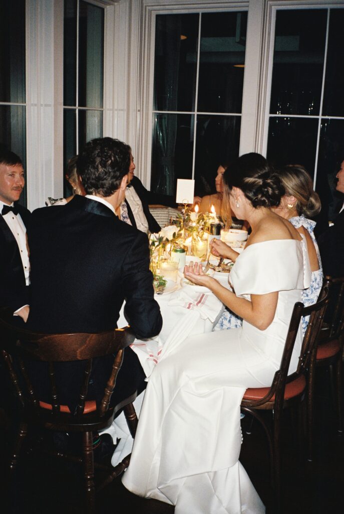 Newlyweds sit at the reception table with their wedding party while eating dinner