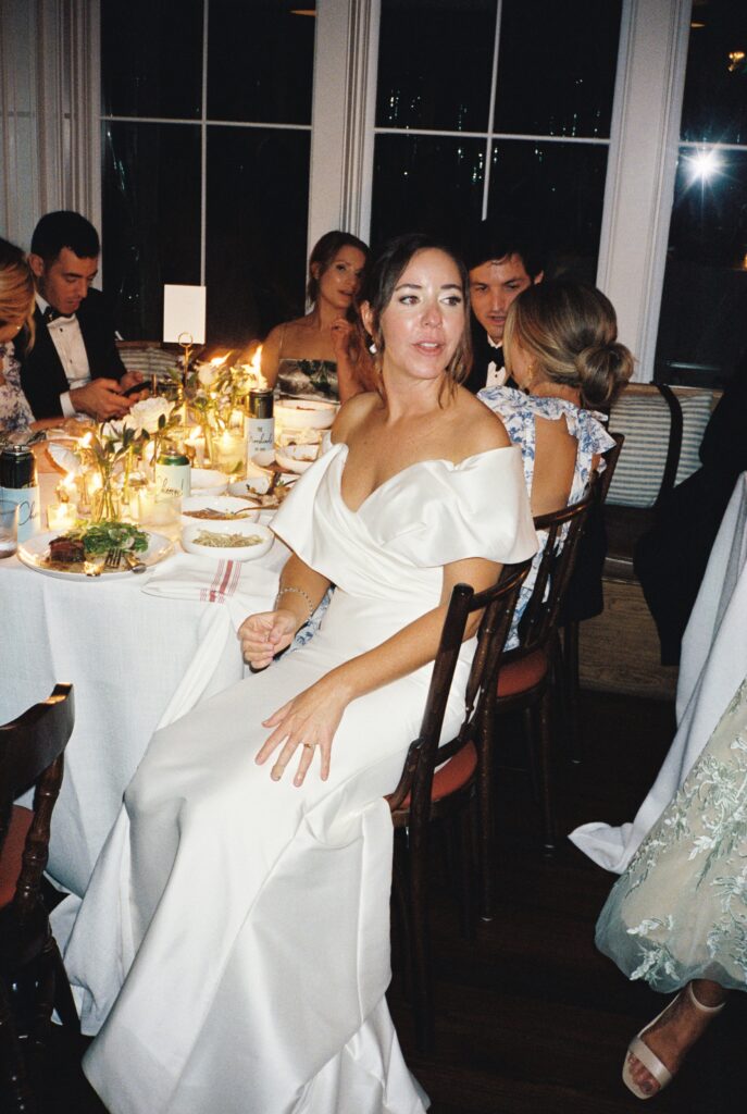 A bride looks over her shoulder while sitting at her Post House Inn wedding reception table to talk with guests