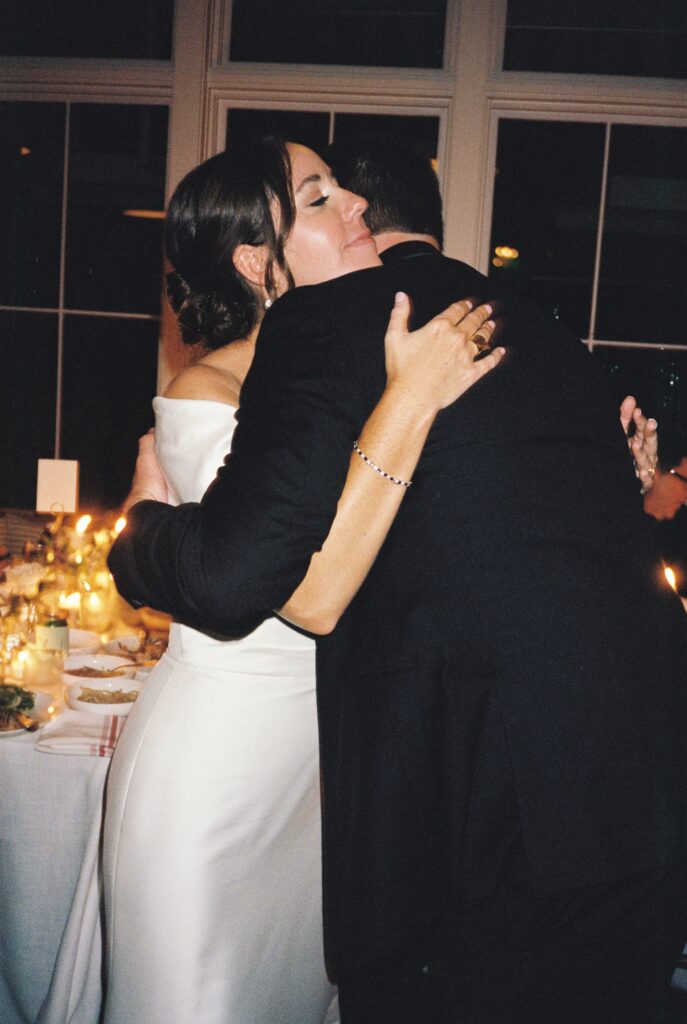 A bride hugs a man in a tuxedo at a wedding reception