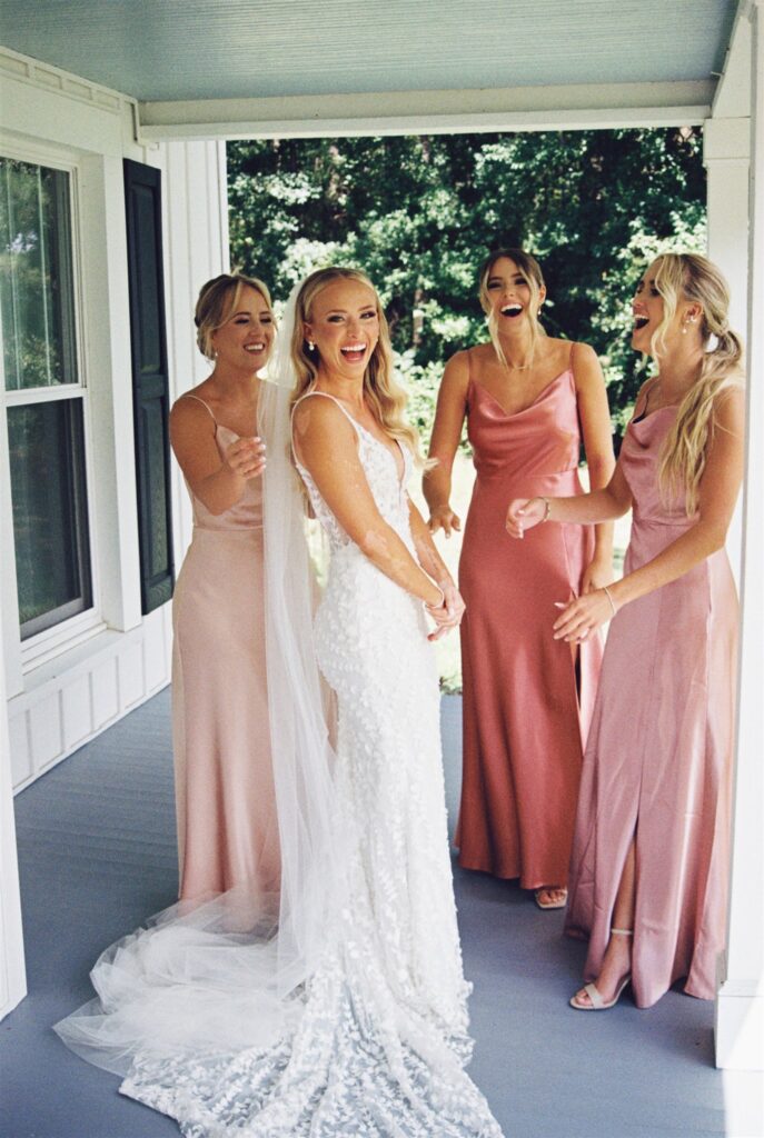 A bride laughs big with her bridesmaids on the porch of one of the Wilmington wedding venues