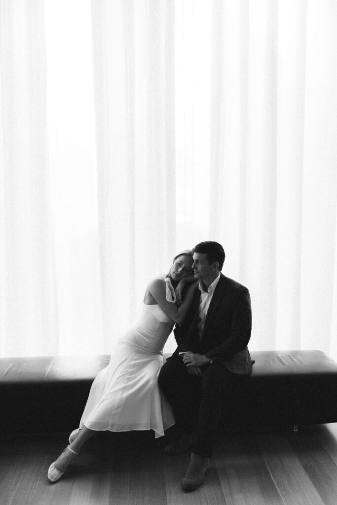 A bride leans on her groom's shoulder in black and white on a leather bench at one of the Wilmington wedding venues