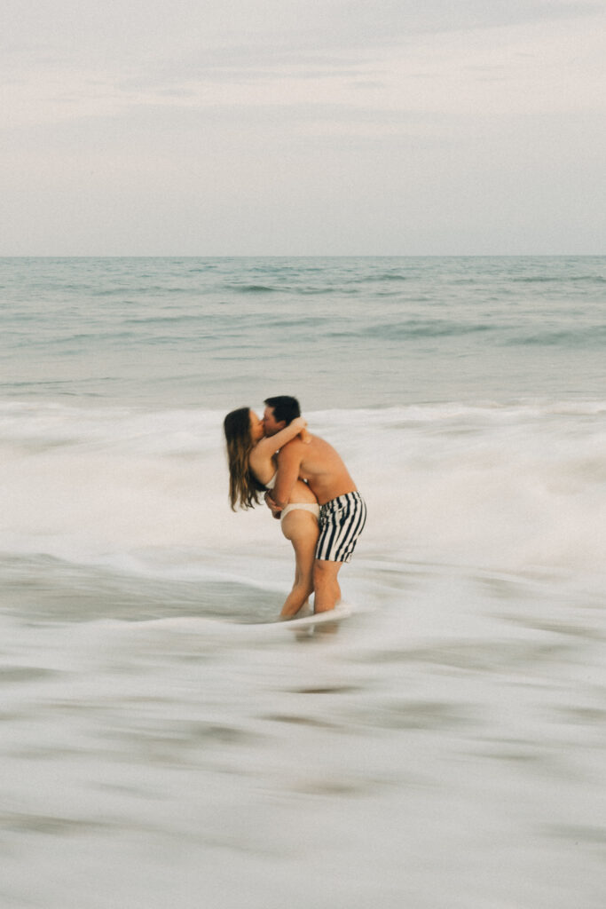 NEwlyweds in bathing suits kiss in the water on the beach