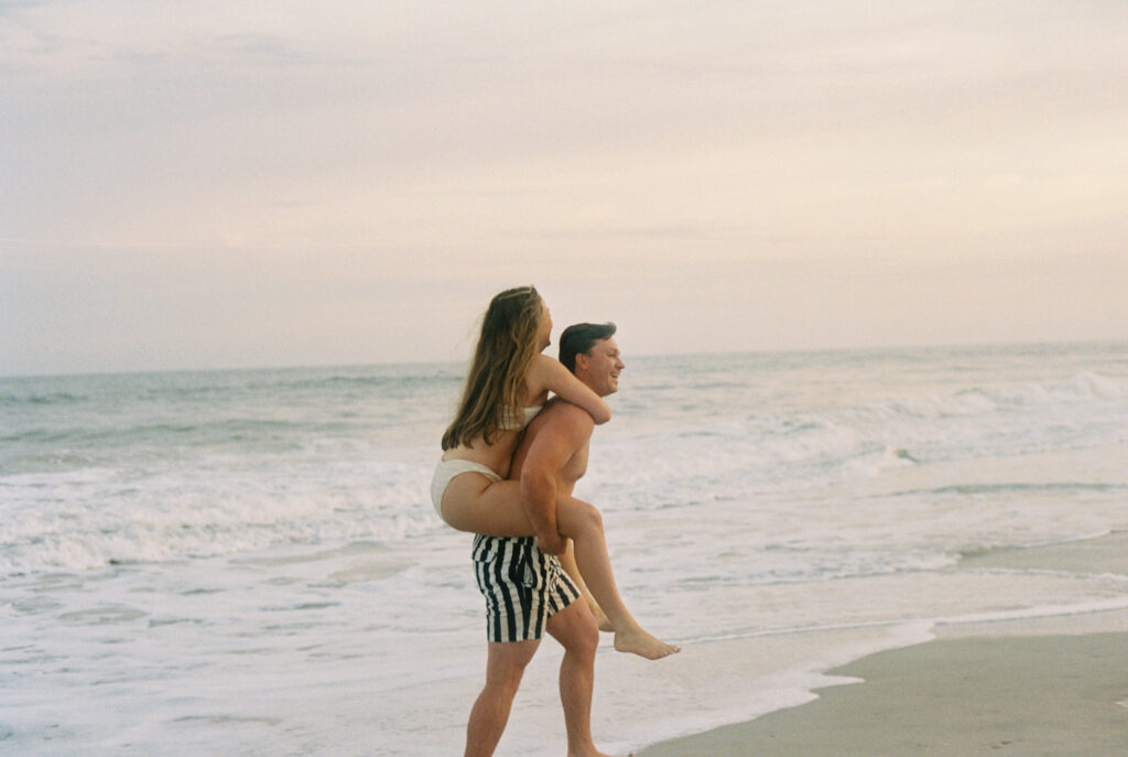 Happy couple on a beach giving the bride a piggy back ride at sunset