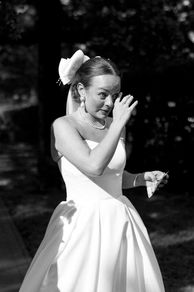 A bride wipes away tears while standing in a garden in black and white