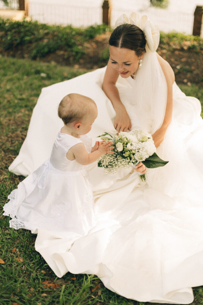 An infant examines a bride's white bouquet in a garden at one of the Wilmington wedding venues