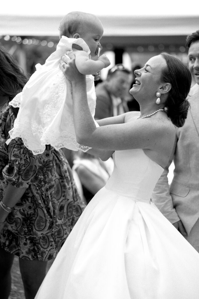 A bride smiles big while lifting an infant in a white gown above her head on the dance floor at one of the Wilmington wedding venues