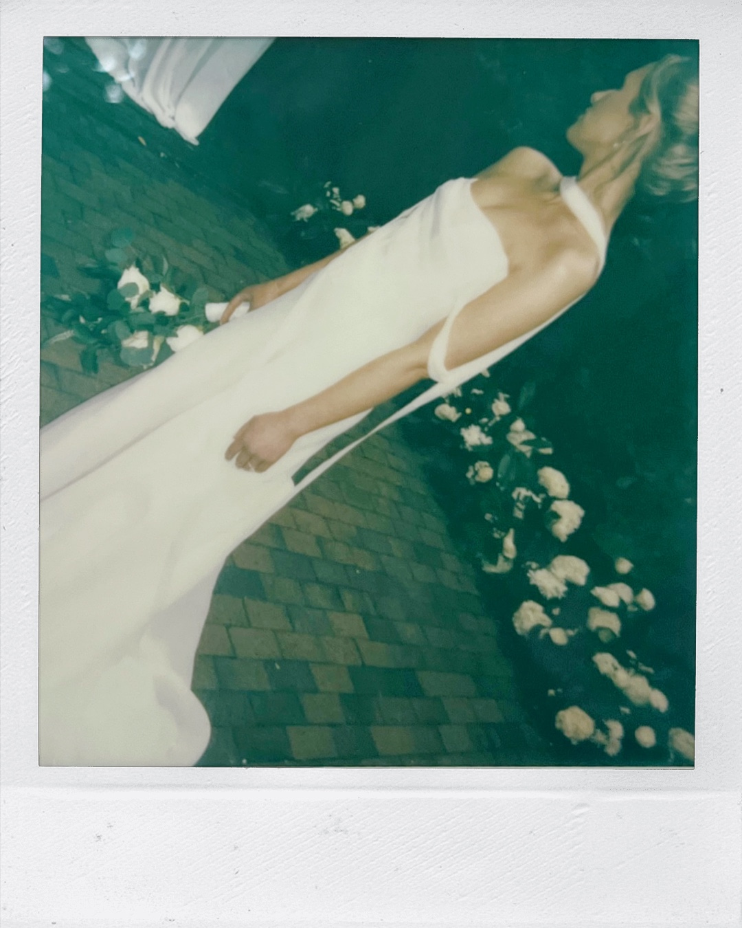 A polaroid of a bride looking over her shoulder holding a white rose bouquet at her side