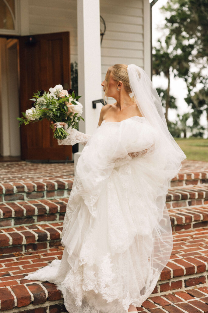 A bride walks down brick stairs holding her train and bouquet