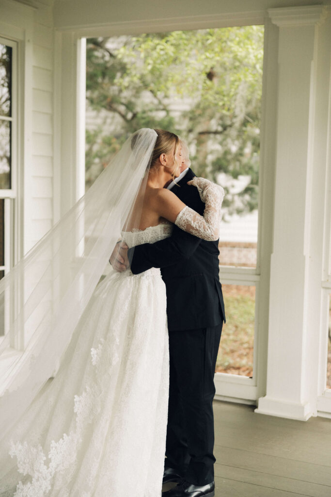 A bride hugs dad during their first look on a porch in his black suit