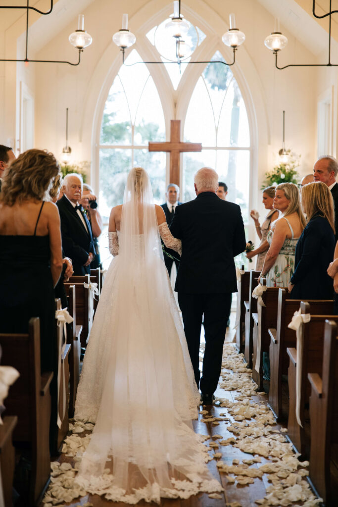 A look down the aisle as a bride walks down with dad as guests watch